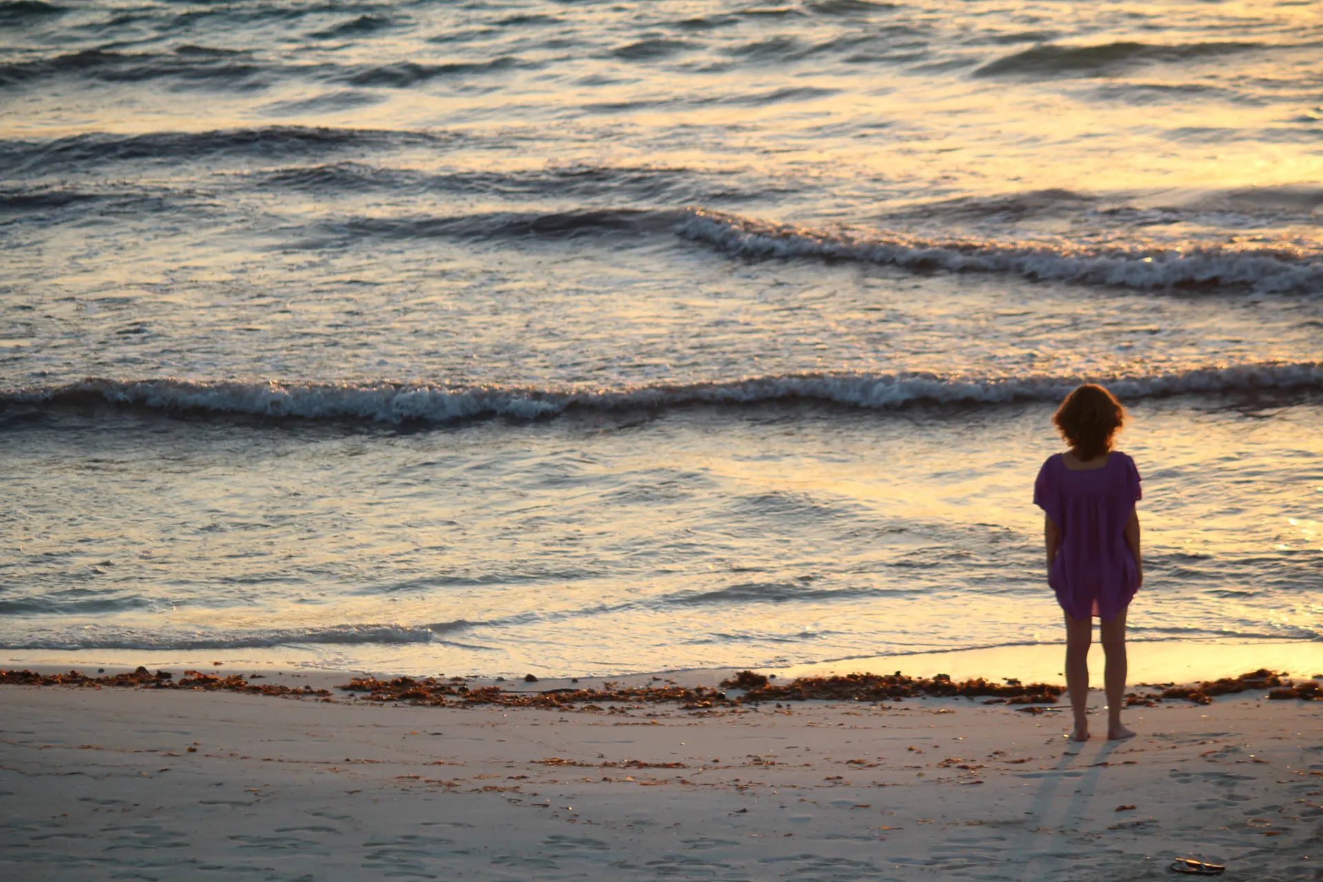 A woman standing at a Finger Lakes shore at sunset near Ithaca, New York, watching the waves, the reflective stillness of nature-based therapy with Laurie Buehler, MFT